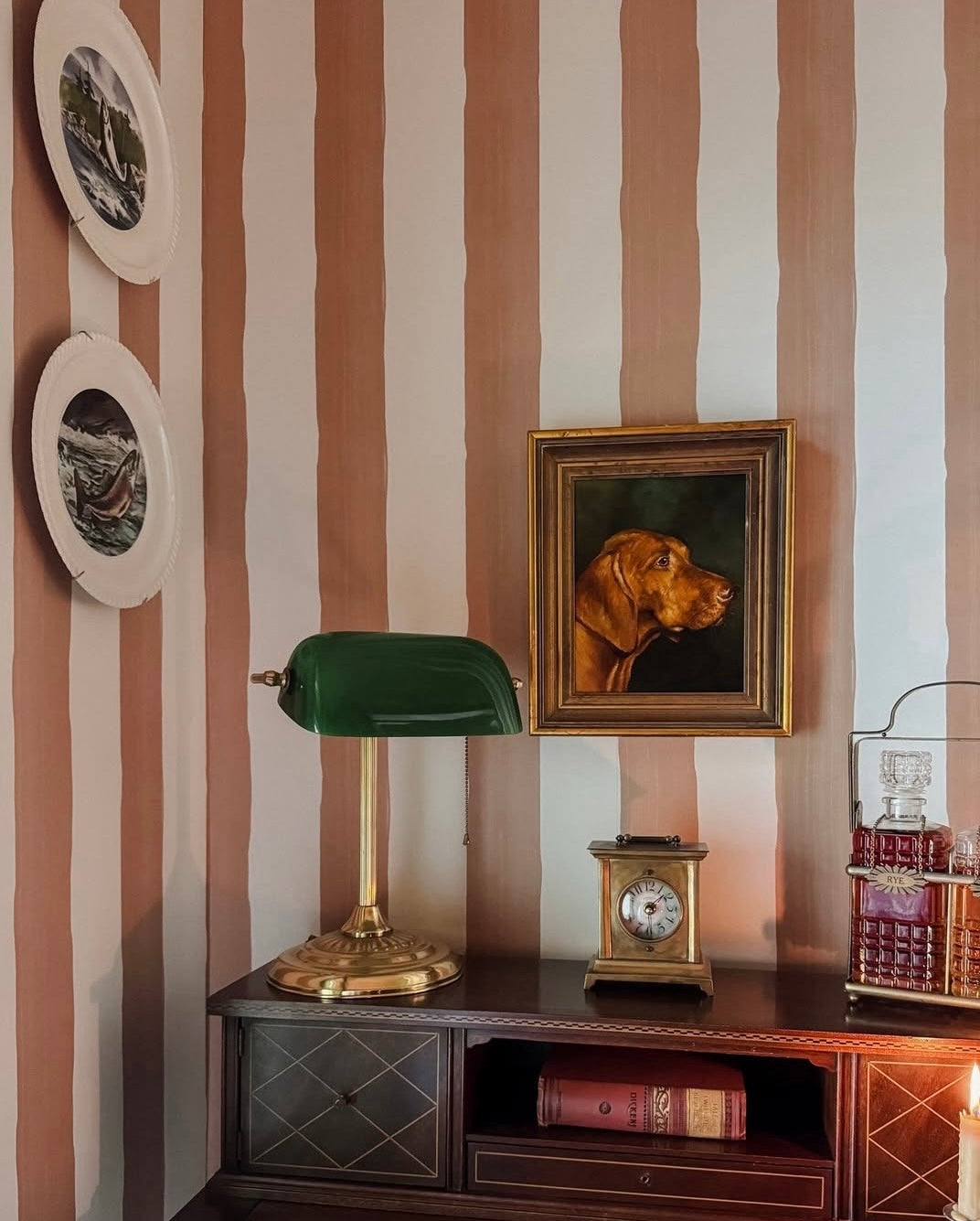 Vintage interior with striped wallpaper, a bankers lamp, and a portrait of a dog.