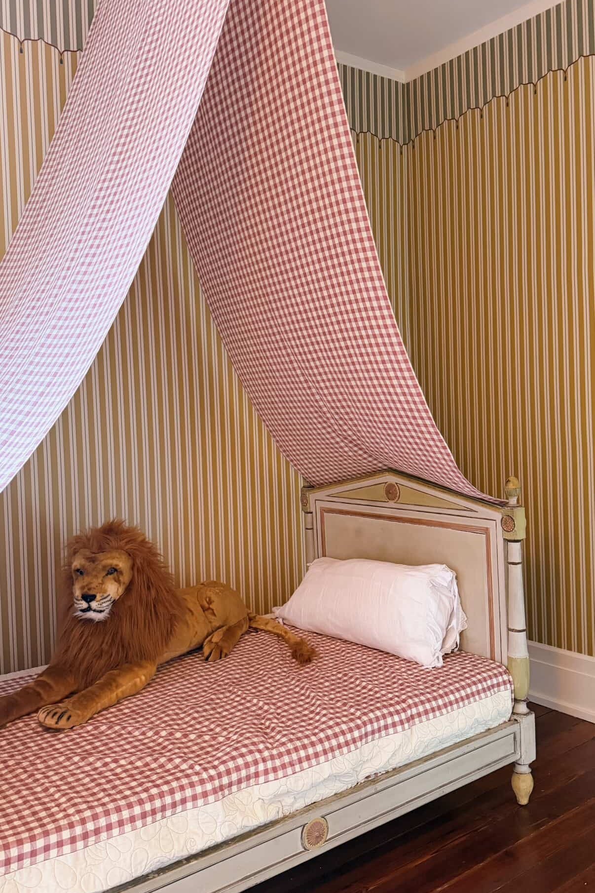 Bed with checkered canopy and lion figurine in a room with striped wallpaper